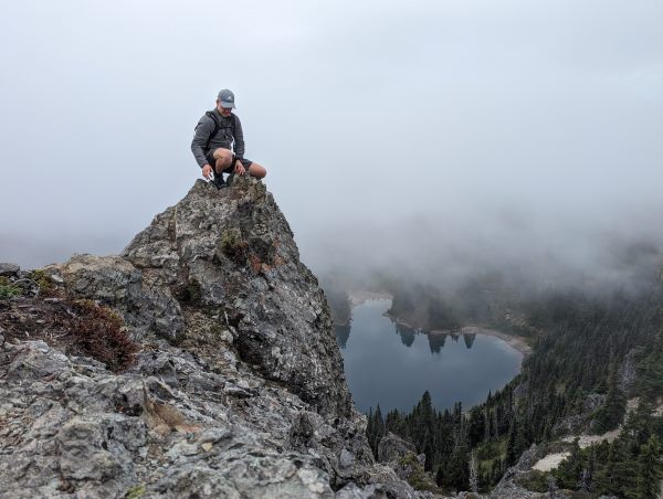 Photograph of Colton balancing on a rock structure with a lake below in the background